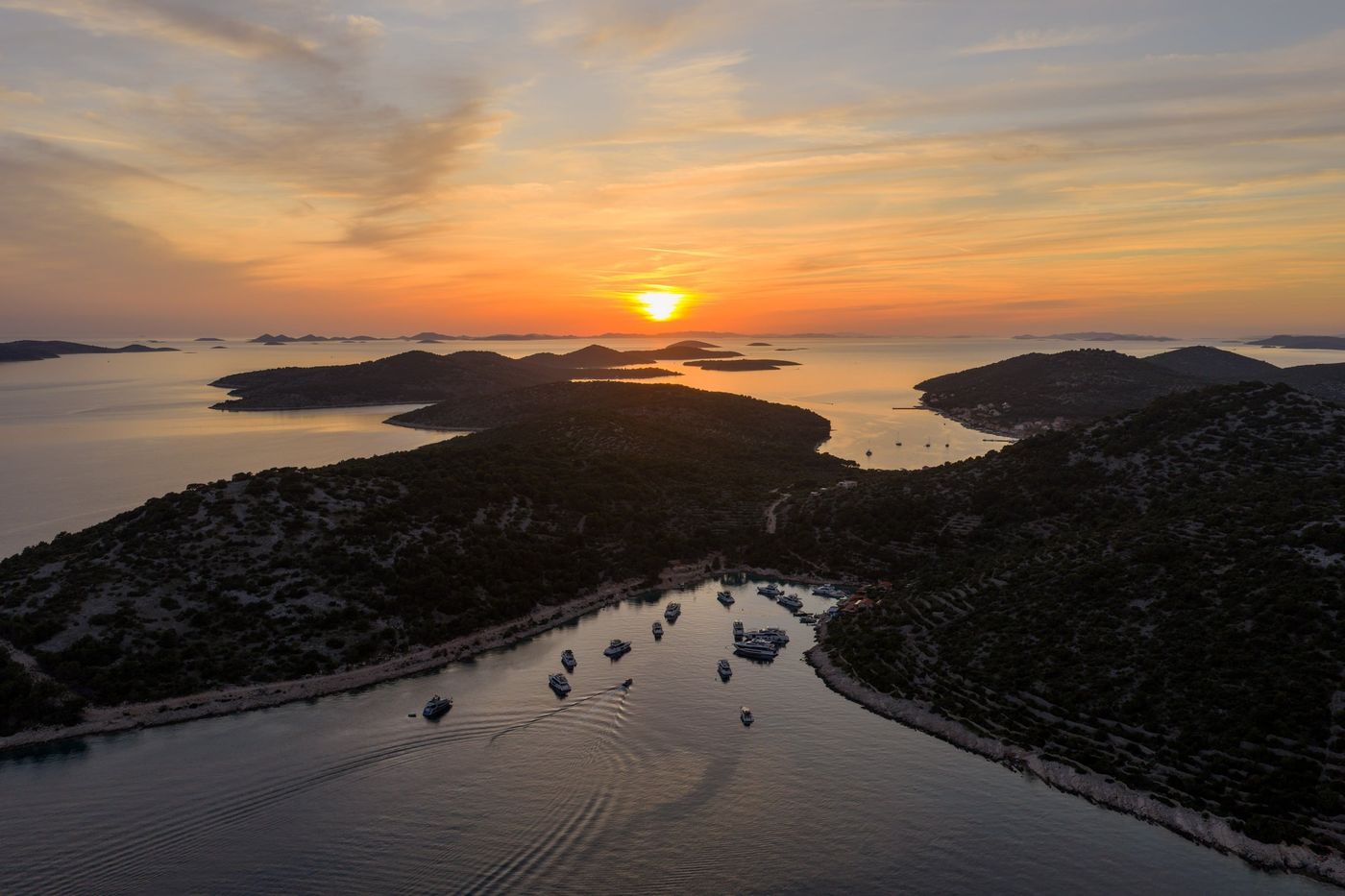 Aerial view at sunset over the Šibenik Archipelago, with yachts anchored in the bay below Kaprije.